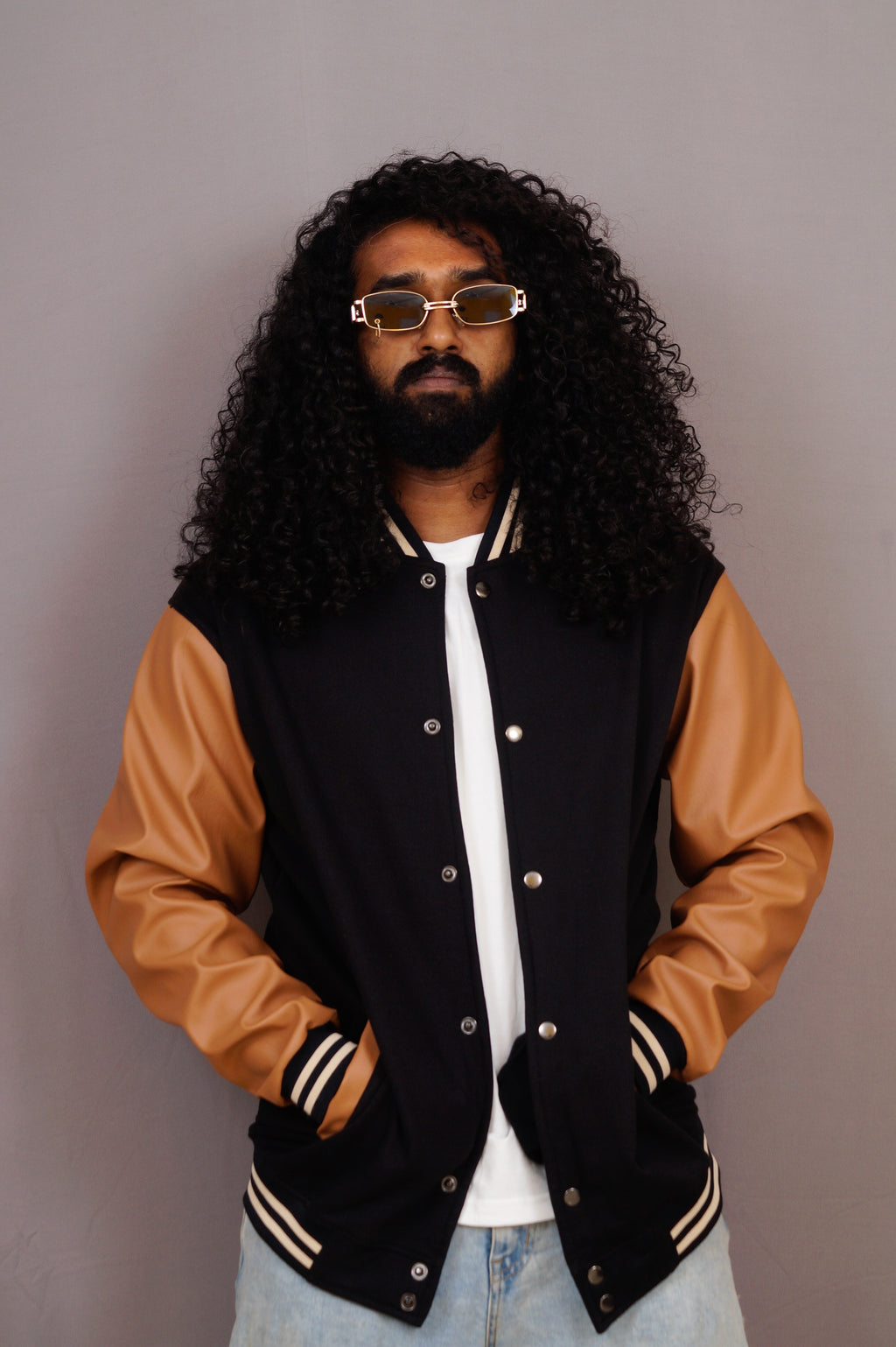 Person wearing a black and brown varsity jacket with a plain background