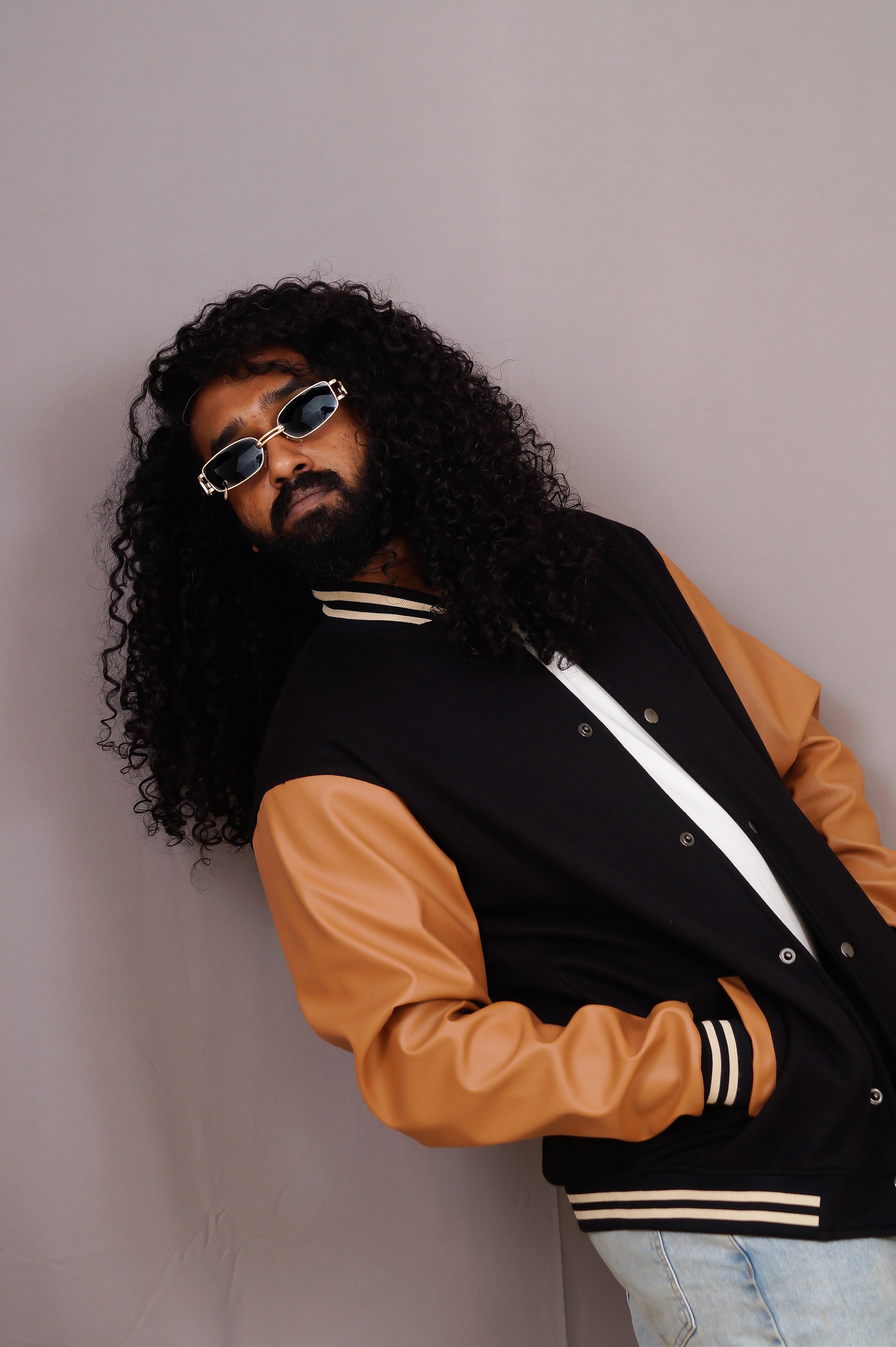 Person wearing a black and brown varsity jacket with sunglasses on a plain background