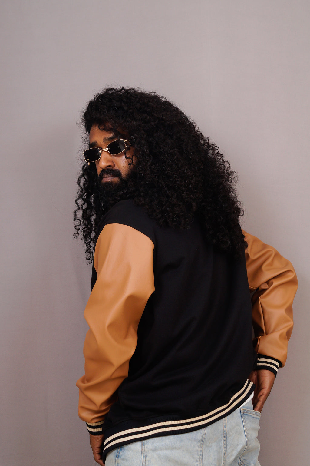 Person wearing a black and brown varsity jacket with sunglasses on a plain background