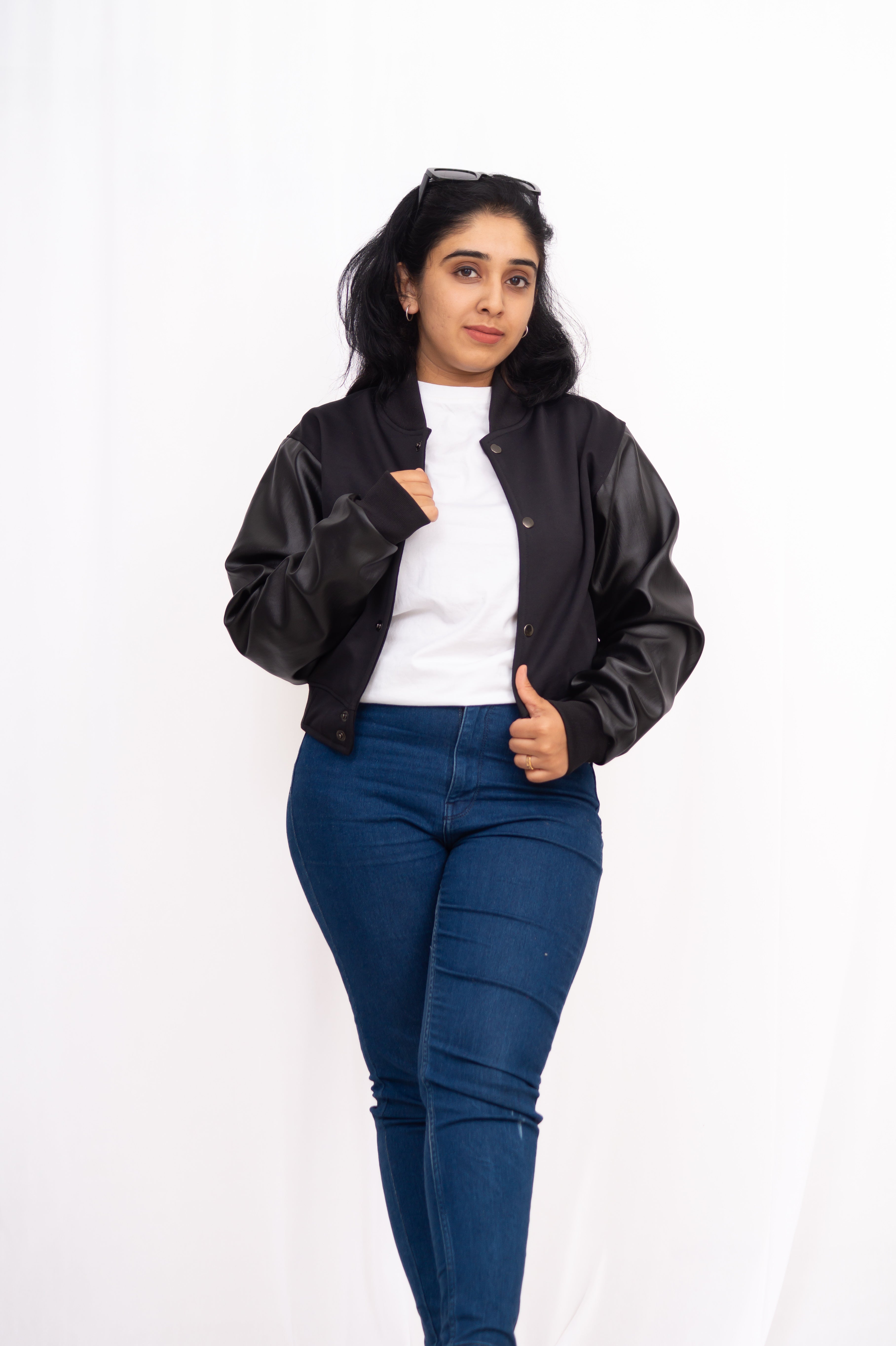 Woman wearing a black bomber jacket, white shirt, and blue jeans on a white background