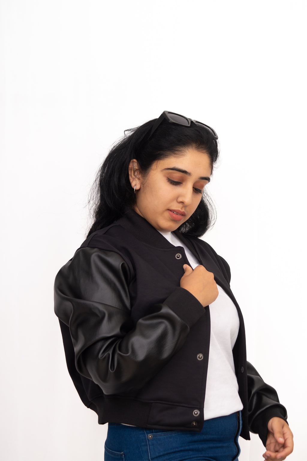 Woman wearing a black varsity jacket over a white shirt on a white background