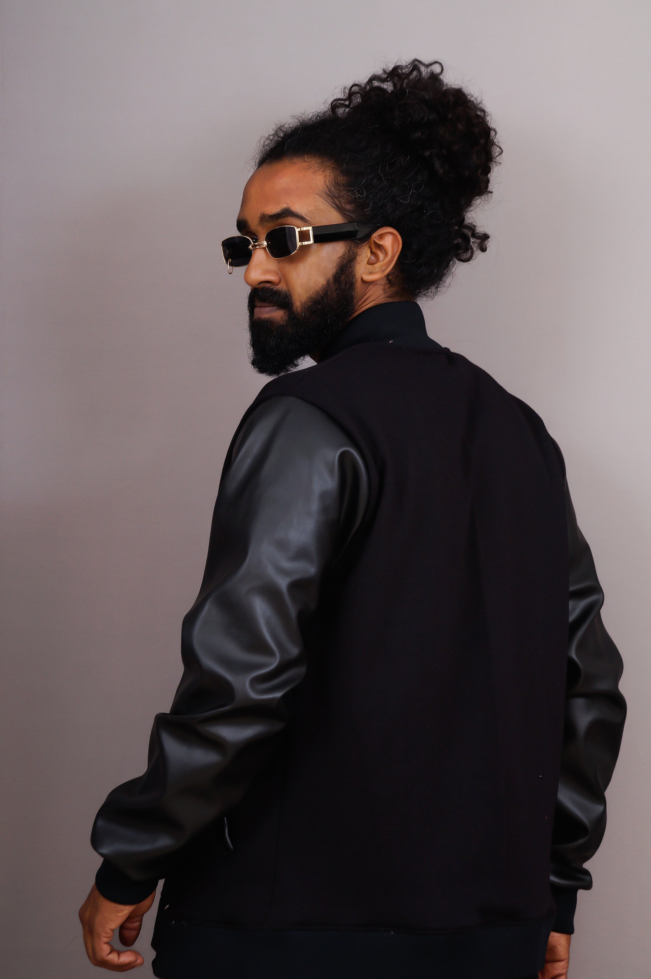 Man wearing a black jacket with leather sleeves against a plain background