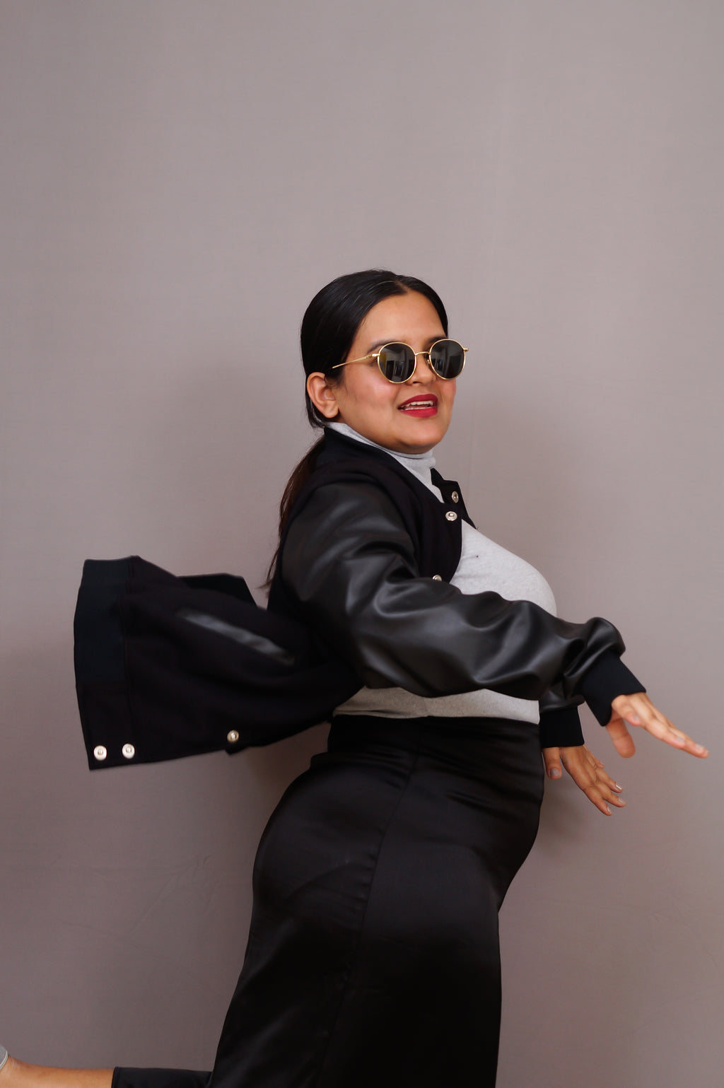 Woman wearing a black leather jacket and sunglasses against a gray background