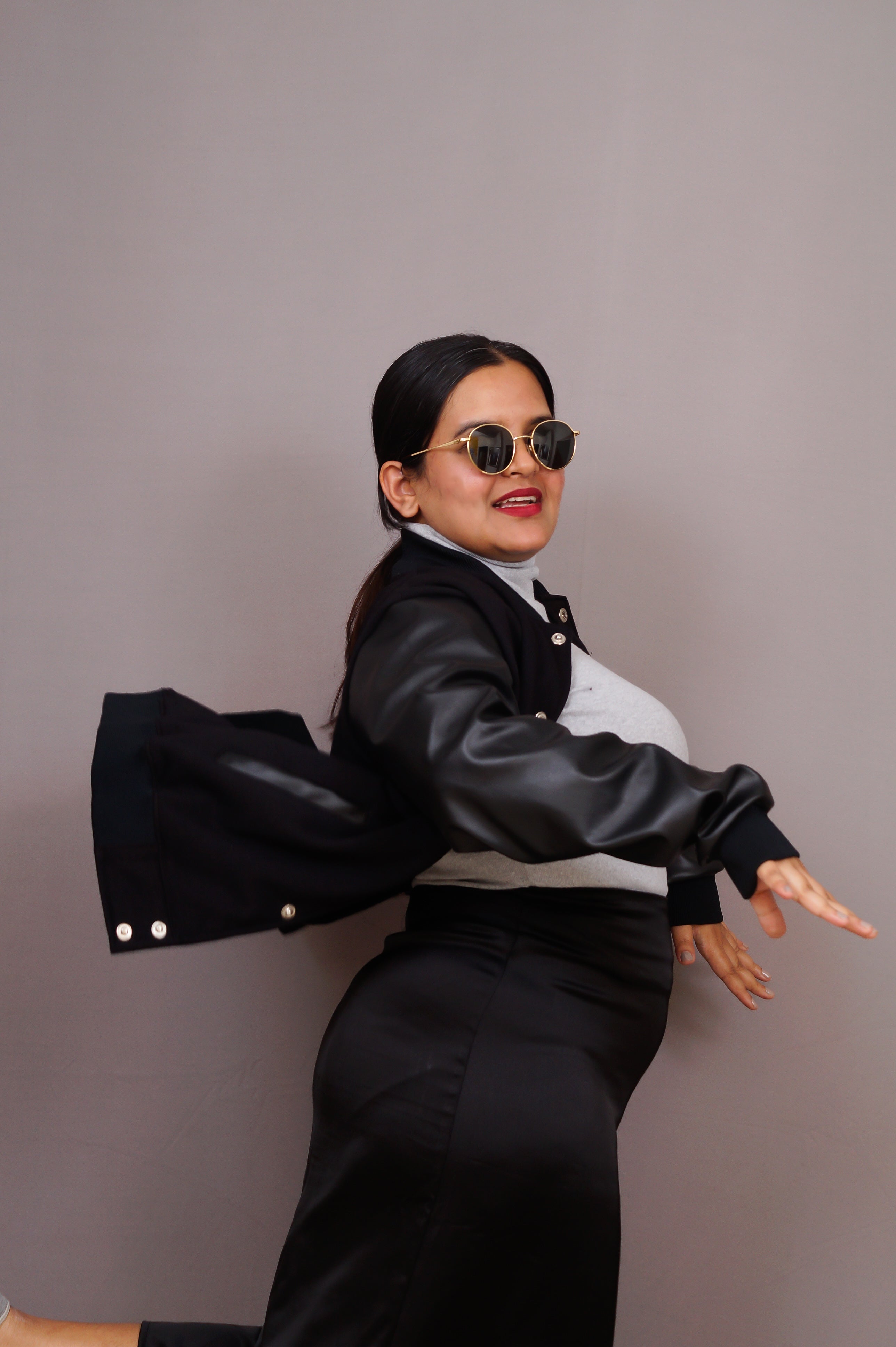 Woman wearing a black leather jacket and sunglasses against a gray background