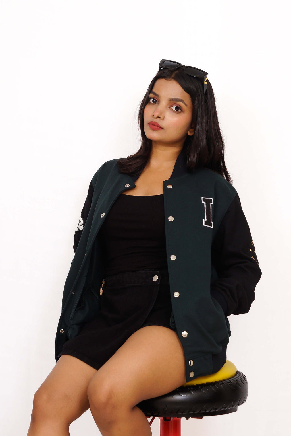 Woman wearing a black varsity jacket with a letter 'I' on a white background