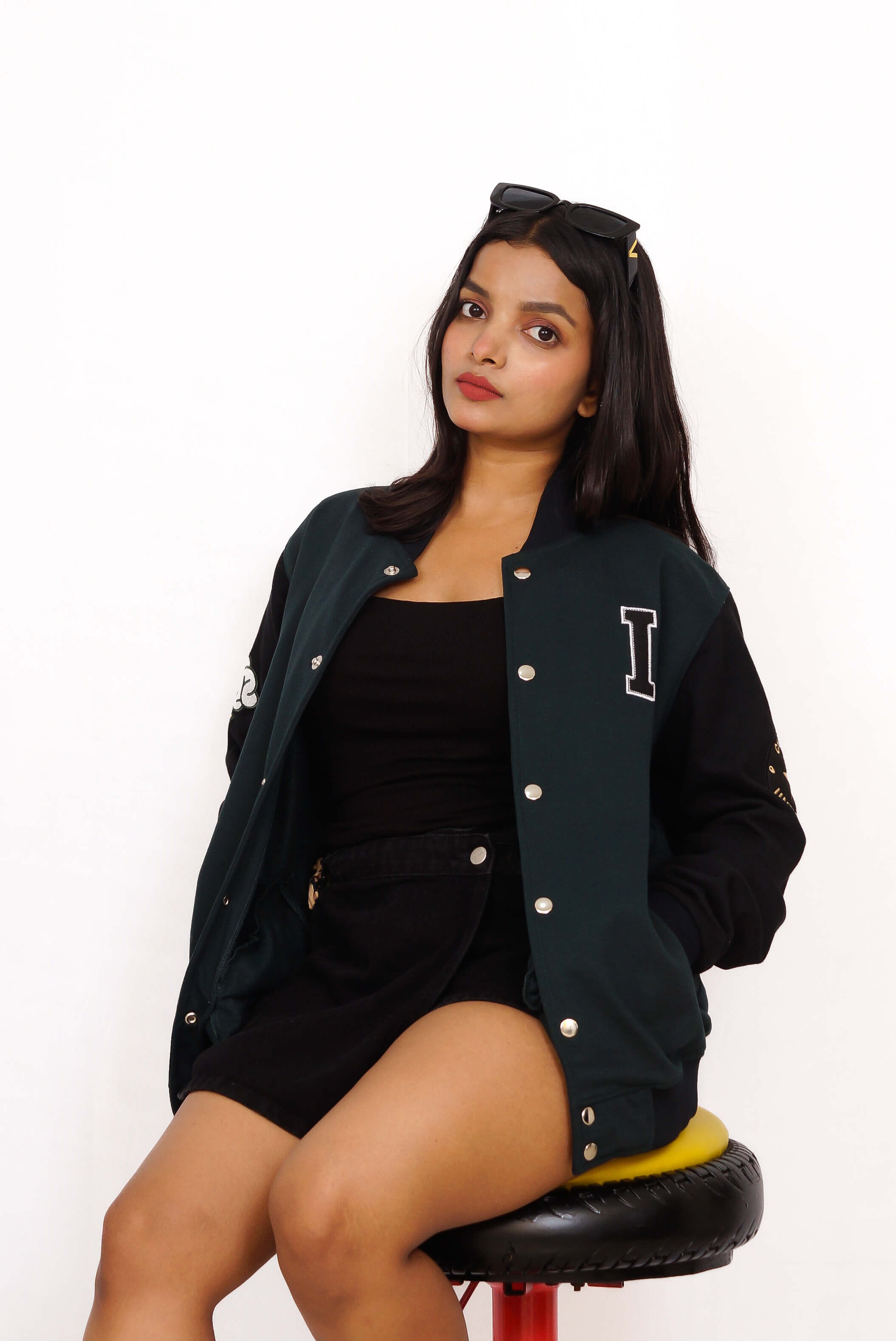 Woman wearing a black varsity jacket with a letter 'I' on a white background